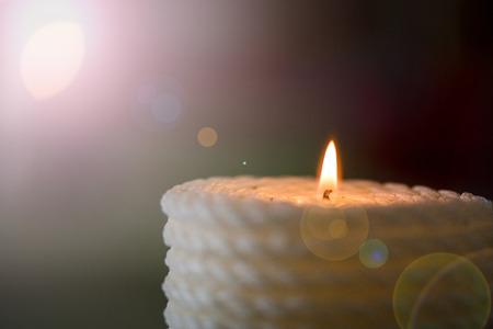 Lit up candle in wicker wooden basket standing on table in restaurant or dining room on green, natural linen tablecloth.の写真素材