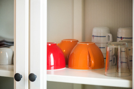 Just washed, clean, colorful cups, glasses, bowls and mugs standing in white cupboard in kitchen. Concept of breakfast and morning coffee and waiting for guests. Welcoming atmosphere at homeの写真素材