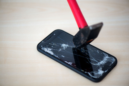 Hammer cracking on smartphone. Screen and display is destroyed, damaged and cracked. Concept of anger, rage and repairing electronic devices. Valid warrantyの写真素材