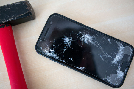 Hammer cracking on smartphone. Screen and display is destroyed, damaged and cracked. Concept of anger, rage and repairing electronic devices. Valid warrantyの写真素材