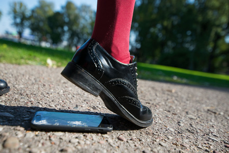 Woman step on the phone. Broken and damaged smartphone with cracks on glass screen laying on ground....
