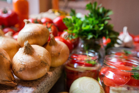 Canning fresh tomatoes with onions in jelly marinade. Woman hands putting red ripe tomato slices and onion rings in jars. Basil, parsley leaves on top of onions. Vegetable salads for winterの写真素材