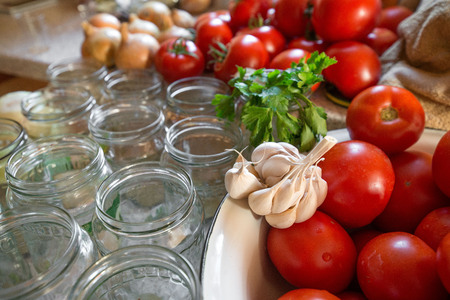 Canning fresh tomatoes with onions in jelly marinade. Woman hands putting red ripe tomato slices and onion rings in jars. Basil, parsley leaves on top of onions. Vegetable salads for winterの写真素材