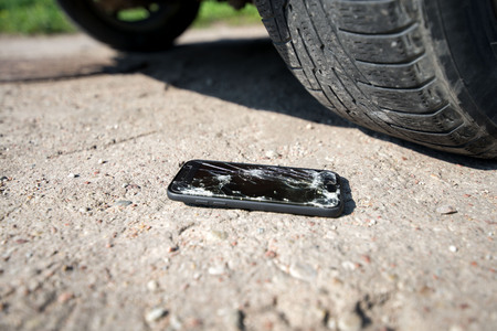 Broken and damaged smartphone with cracks on glass screen laying on ground. Accident. Cell phone...