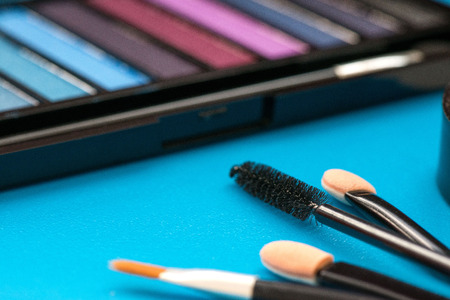 Top, up view of professional cosmetics, makeup background. Brushes, eye shadows, eyebrow pencils, powder, bronzing balls, mascara, red lipstick. Tools isolated on blue. Concept of get ready for partyの写真素材