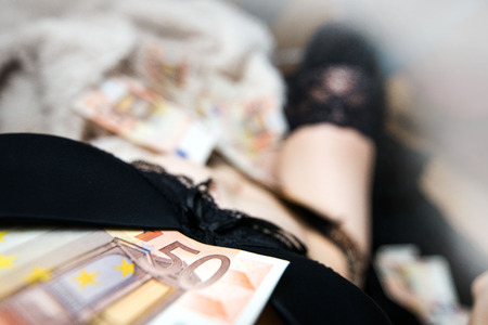 Woman in lingerie with large number of euro money laying on bed. Half naked body. Concept of dirty moneyの写真素材