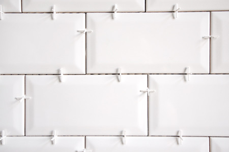 Ceramic tile lying. Installing new subway or metro tile in bathroom, shower or kitchen back splash during home renovation. Placing or taking out tile spacers with hands and pliers.の写真素材
