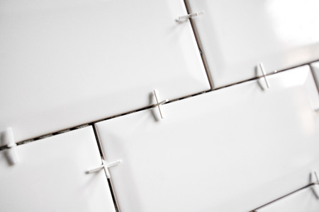 Ceramic tile lying. Installing new subway or metro tile in bathroom, shower or kitchen back splash during home renovation. Placing or taking out tile spacers with hands and pliers.の写真素材