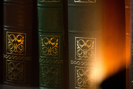 Old vintage style books in a row in a shelf in living room. Concept of knowledge, education and reading books. Cozy atmosphere in house or apartment with warm light reflectionの写真素材