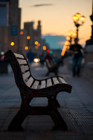 Empty wooden bench in Bari, Italy. Busy street and traffic with cars anr lights in background. Concept of lonelinessの写真素材