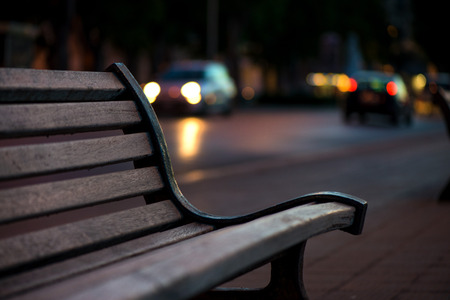 Empty wooden bench in Bari, Italy. Busy street and traffic with cars anr lights in background....