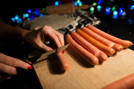 Preparing tanned wiener sausages in pizza dough. Cutting sausages on wooden board before baking....