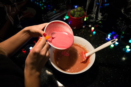 Woman is cooking in kitchen, baking a red velvet cake. Using red food coloring in dough. Concept of...