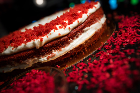 Woman sprinkling raspberry crumbs, icing sugar over freshly made cake, creating ornaments and decorating dessert. Beautiful home made red velvet cake decorated with whipped cream and raspberry crumbsの写真素材