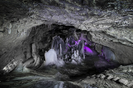 Underground glacier in Glaciers Cave in Apuseni mountains, Scarisoara, Romania. Ice and big icicles with colorful back light. Stalactites and stalagmites in dark caveの写真素材
