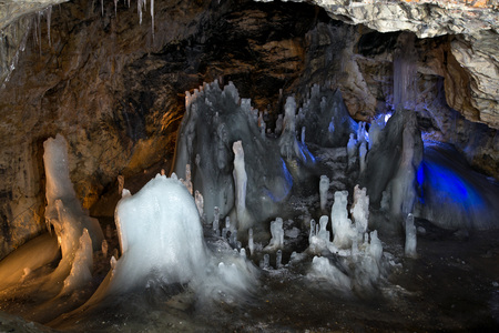 Underground glacier in Glaciers Cave in Apuseni mountains, Scarisoara, Romania. Ice and big icicles with colorful back light. Stalactites and stalagmites in dark caveの写真素材