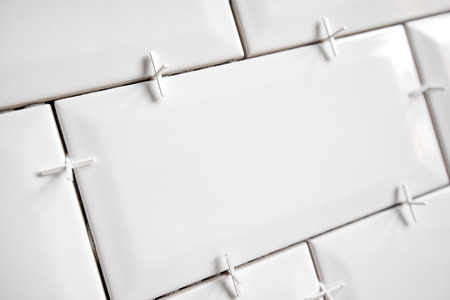 Ceramic tile lying. Installing new subway or metro tile in bathroom, shower or kitchen back splash during home renovation. Placing or taking out tile spacers with hands and pliers.の写真素材