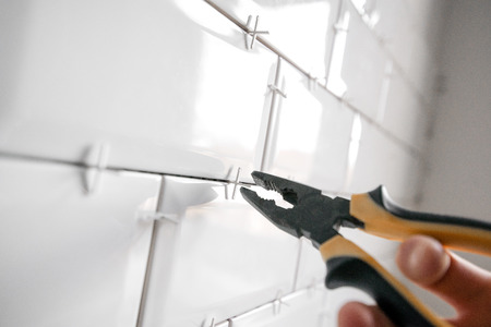 Ceramic tile lying. Installing new subway or metro tile in bathroom, shower or kitchen back splash during home renovation. Placing or taking out tile spacers with hands and pliers.の写真素材