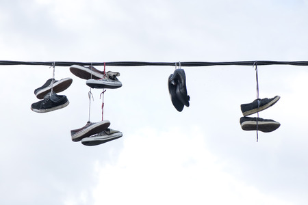 Old sneakers and high heel shoes hanging on electrical wire on overcast background.の写真素材