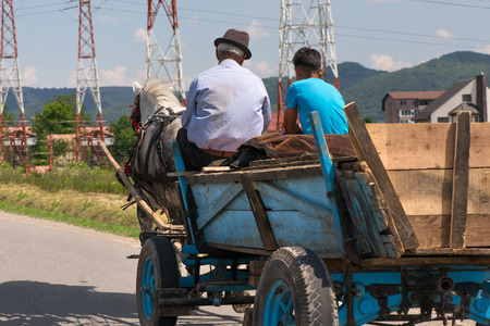 Traditional transylvanian horse is walking through Romanian village,  Concept of hard working animals. Man and his son sitting in wooden cart pulled by a horse. Peasants on a horse-drawn carriageの写真素材