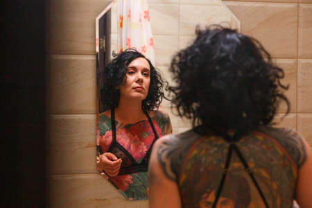 Beautiful young woman combing hair in front of her bathroom mirror. Selective focus.の写真素材