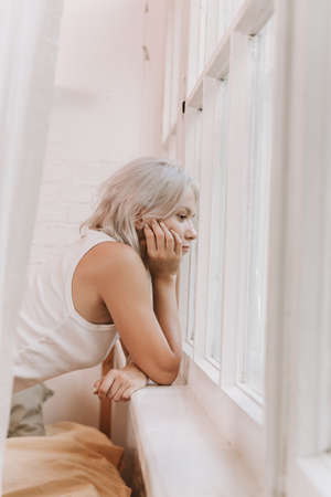 Beautiful woman opening curtains and looking through the windowの写真素材