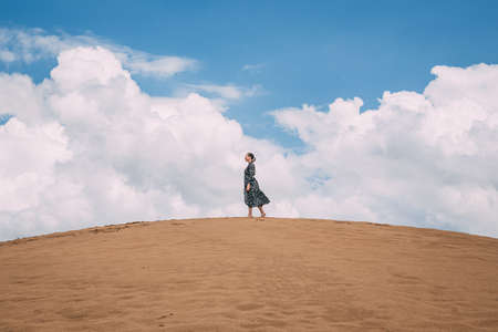 Beautiful landscape in sand dunes. A girl in a pink light dress walks through the desert against the blue sky. Safari in Kazakhstan. Golden Sands of Mangystau at sunsetの写真素材