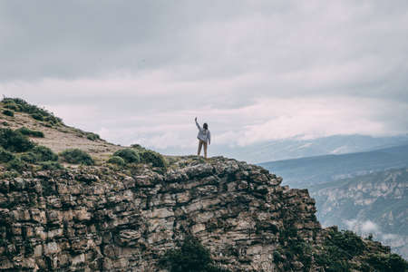 A young traveling woman stands on the edge of a mountain cliff and watching a beautiful view of the...