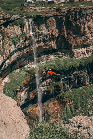 Young athlete hanging from a slackline. Highline between cliffs in the mountains, in a beautiful scenery on a sunny dayのeditorial素材