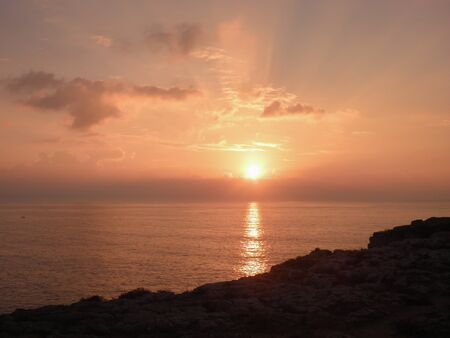 pinkish image of sunset on the sea with clouds in the sky and the reflection of the sun on the waterの写真素材