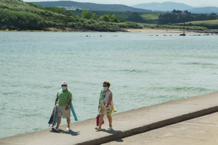 Suances, Cantabria / Spain; 07 14 2020: Couple keeping safe from the coronavirus from a distance and with a mask on the bank of the Pas River just before its mouthのeditorial素材