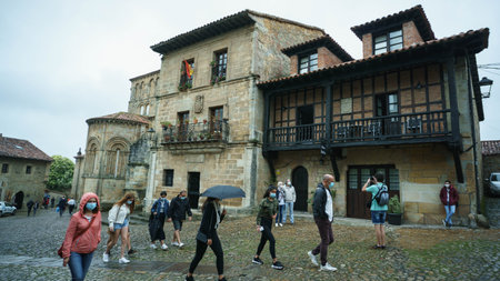 Santillana Del Mar, Cantabria / Spain; 07 15 2020: Several tourists wearing a protective mask for the coronavirus doing rural tourism in one of the most beautiful villages in Spain on a rainy dayのeditorial素材
