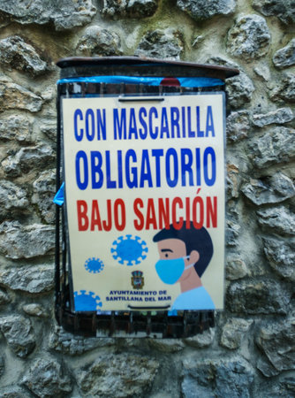 Santillana Del Mar, Cantabria / Spain; 07 15 2020: sign of obligatory use of the mask in front of the danger of the coronavirus in a fence of a small very tourist townのeditorial素材