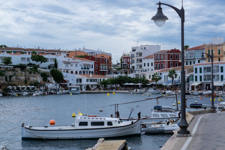 Es Castell, Balearic Islands / Spain; 09 29 2015: Pedestrian port in a small bay with an old pier, small boats all along the shore and a promenade all around under the picturesque villageのeditorial素材