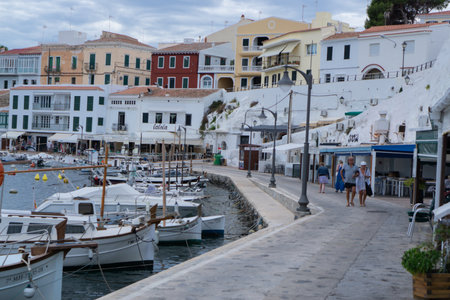 Es Castell, Balearic Islands / Spain; 09 29 2015: Couples walking through the fishing district of Cales Fonts between the old pier full of small boats and the restaurants built on the rocksのeditorial素材