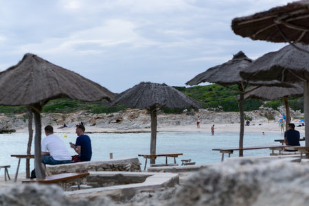 Sant LluÃ­s, Balearic Islands / Spain; 09 29 2015: Different people on a tropical beach with white sand and clear waters surrounded by green vegetation. All this seen from the terrace of a beach bar.のeditorial素材