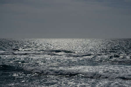 Grayish background of the horizon between a dull sky and the silvery sea by the reflection of the sun when it starts to get darkの写真素材