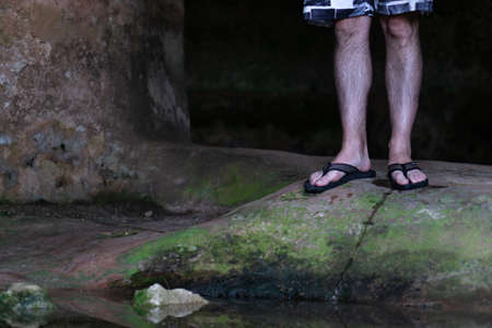 Men's legs in swimsuits and flip-flops on the green stone floor just before a puddle of waterの写真素材