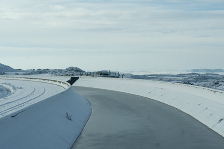 Curved artificial channel of frozen water, surrounded by a wild landscape all snowy.