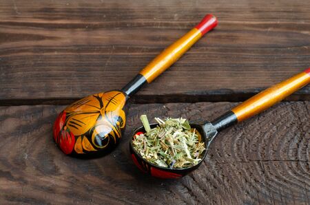 Two slavic wooden spoons. One with herbal medicine. Wooden background.の写真素材
