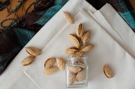 almonds in nutshell from small glass bottle on white linen. Top view