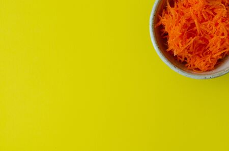 Grated carrot in bowl on yellow background with copy space. Top view.の写真素材