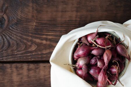 Red seeding-onion in bowl and white linen on wooden background. Top view with copy space