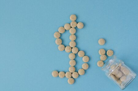 Dollar sign made of pills. Herbal antiviral pills from small glass bottle on blueの写真素材