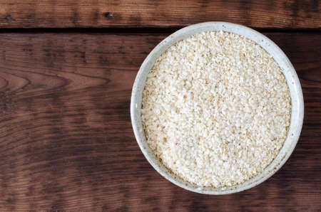 Sesame oilcake. Squeezed white sesame in clay glazed bowl on wooden background. Benne. Top view.の写真素材