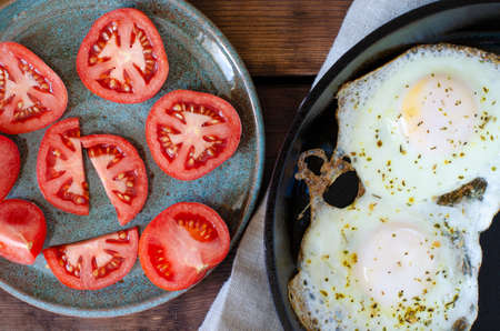 sliced tomatoes on plate. Fried eggs on frying pan on linen and wooden background.の写真素材