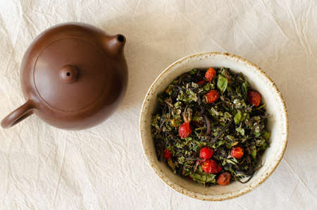 herbal mix in clay cup and clay teapot on linen background. Hips and raspberry leaves. Top view.の写真素材