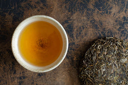 green puer tea. Pressed tea leaves and clay cup on abstract wooden backdrop.の写真素材