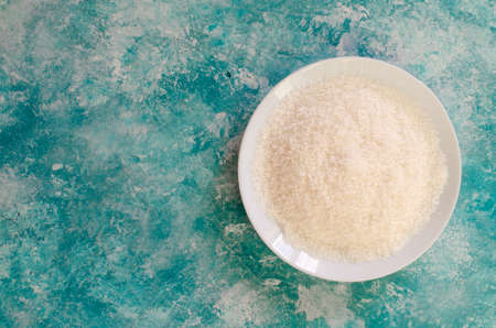 Fresh coconut flakes on white plate on abstract aqua blue background. Top view.の写真素材