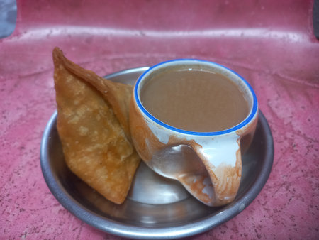 A small steel plate with one potato samosa and a cup of teaの写真素材